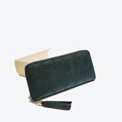 Pochette portefeuille vert eélégante avec des coutures apparentes. Pochette posé sur une table contre un support blanc devant une photo