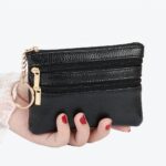 Main de femme tenant un portefeuille noir avec des fermetures éclair et un porte-clés sur fond blanc.
