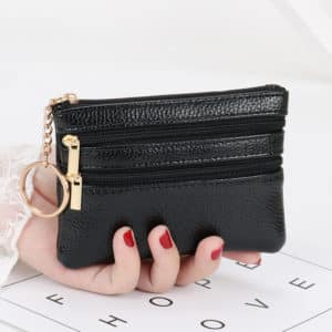 Main de femme tenant un portefeuille noir avec des fermetures éclair et un porte-clés sur fond blanc.