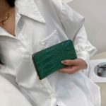 Portefeuille zippé long en cuir verni vert crocodile, tenu par une main de femme