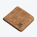 Portefeuille couleur camel carré posé sur une surface en bois. Il y a un logo noir en bas à droit du portefeuille.