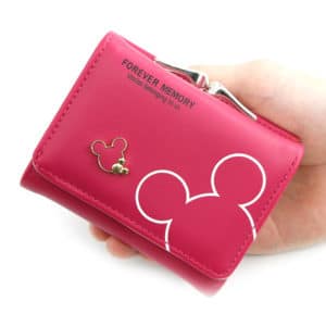 Portefeuille rose fushia avec les contours de la silhouette de mickey de couleur dorée. Le portefeuille est tenu par une mains sur la droite.