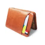 Portefeuille marrone en cuir posé en forme de V sur un fond blanc et avec des cartes qui dépassent de la poche exterieure.