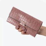 Portefeuille rose crocodile tenu dans une main de femme