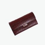 Grand portefeuille rouge aspect crocodile et fermoir doré. Fond en marbre et magazine ouvert.