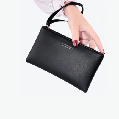 Main avec du vernis rouge qui tient un portefeuille uni noir du bout des doigts. Sangle autour du poignet. La femme est habillée en blanc