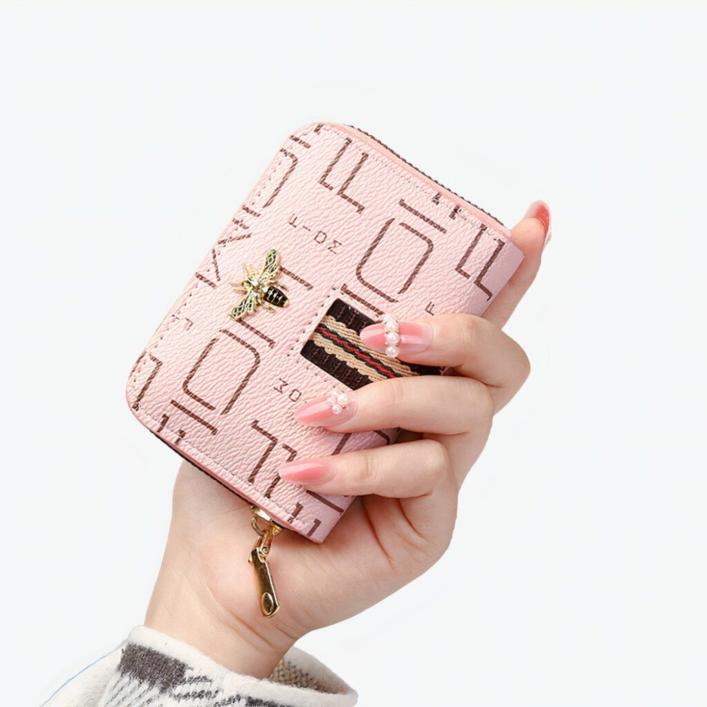 Main de femme tenant un petit portefeuille rose avec des motifs sur fond gris.