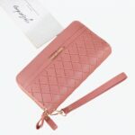 Pochette rose avec une sangle sur le côté posé sur un table couleur rose saumon. Au dessus de la pochette se trouve des feuilles blanches;