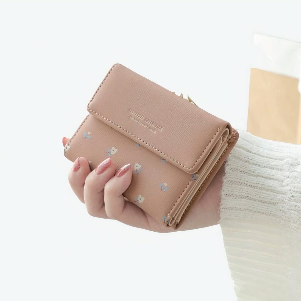 Joli petit portefeuille en simili-cuir de couleur beige, très féminin tenu dans la main d'une femme qui porte du vernis et un pull blanc.