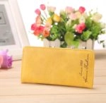 Joli chéquier portefeuille jaune de 18x9 cm, posé sur une table près d'un cadre et d'un bouquet de fleurs.