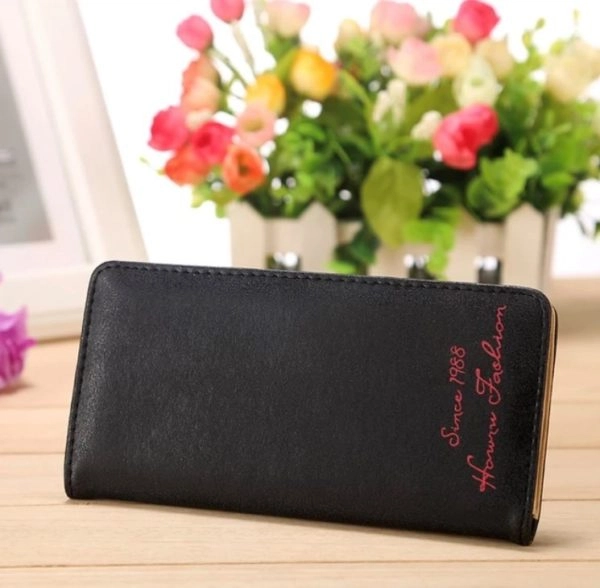 portefeuille porte chéquier noir avec une inscription rose. Il est posé sur une table près d'un bouquet de roses.