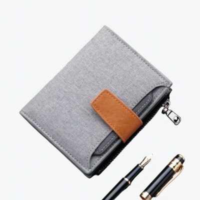 Portefeuille en toile grise avec fermeture en cuir synthétique marron. Au fond, on voit un clavier d'ordinateur et des stylos au premier plan.