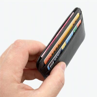 Main tenant un petit portefeuille noir vu depuis la tranche. Il contient des cartes. Fond blanc.