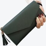 Pochette portefeuille vert avec un pompon tenue dans une main