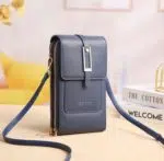 Magnifique sac portefeuille en cuir synthétique bleu. Finitions dorées, emplacement pour accès rapide au téléphone. Il est posé sur une table près de livres de déco.