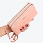 Portefeuille rose pâle tenu dans une main avec du vernis rouge