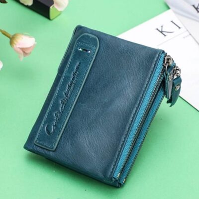 Portefeuille bleu turquoise sur fond vert avec des roses et une feuille blanche derrière le portefeuille