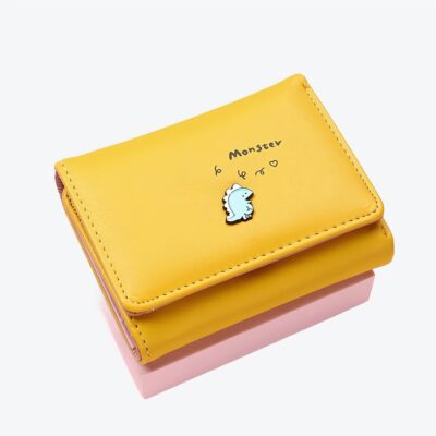 Portefeuille carré jaune sur fond rose avec un petit monstre bleu dessiné dessus.