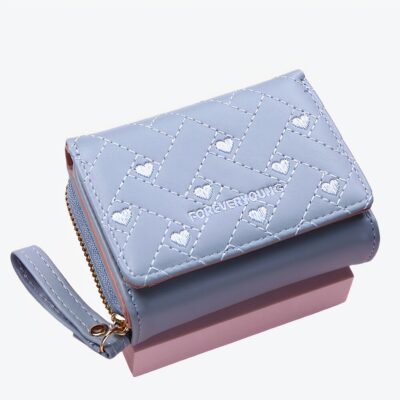 Petit portefeuille bleu avec une sangle et des petits coeurs sur le devant, sur fond rose.