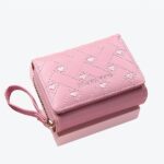 Petit portefeuille rose avec une sangle et des petits coeurs sur le devant, sur fond rose.