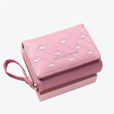 Petit portefeuille rose avec une sangle et des petits coeurs sur le devant, sur fond rose.