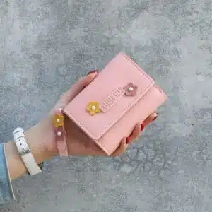 Main tenant un portefeuille rose carré avec des fleurs colorés dessus.